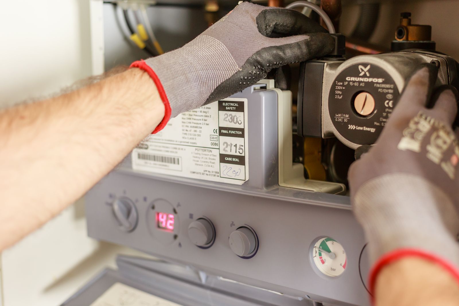 Technician's gloved hands servicing the internal controls of a home heating system